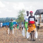People receiving aid supplies in a rural African community with a truck in the background.